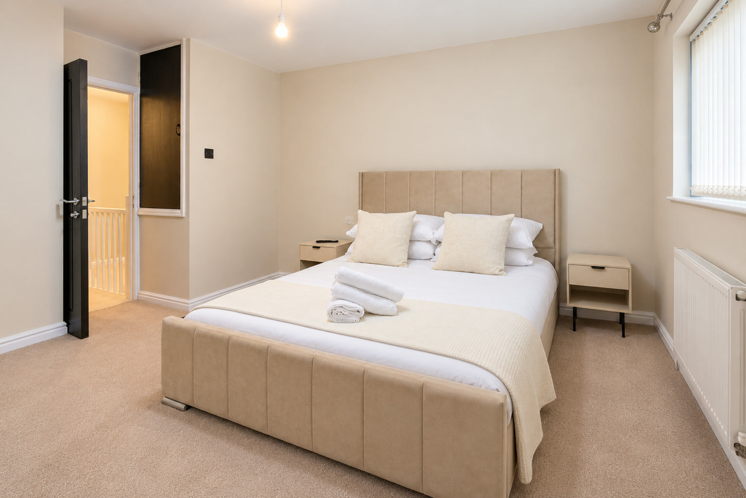 A guest bedroom with an upholstered cream bed, white linen and daylight from the window.