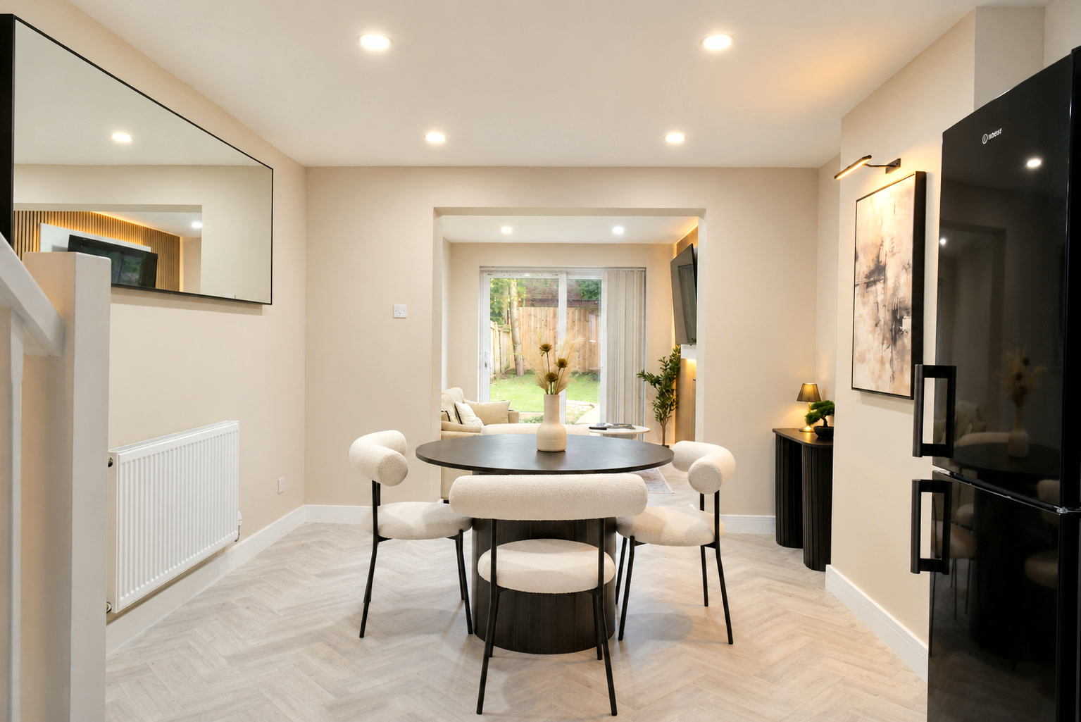 A round black dining table with cream chairs, looking through to the lounge and garden.