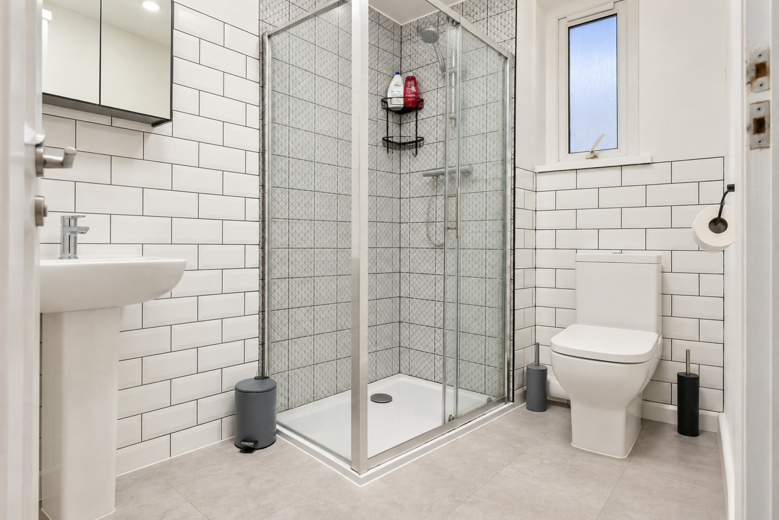 A white tiled shower room with glass enclosure, pedestal basin and closed toilet.