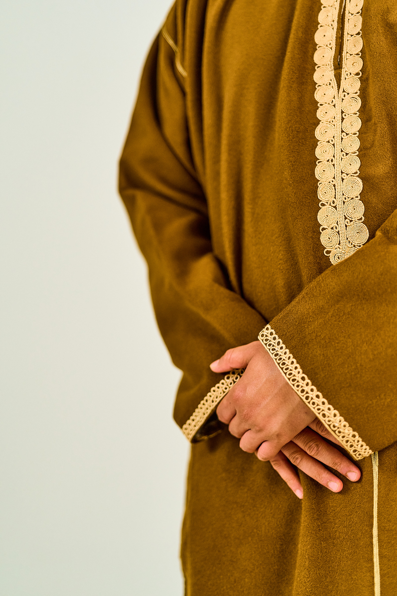 Warm ochre fabric, cream embroidered trim and relaxed hands in a close garment photograph.